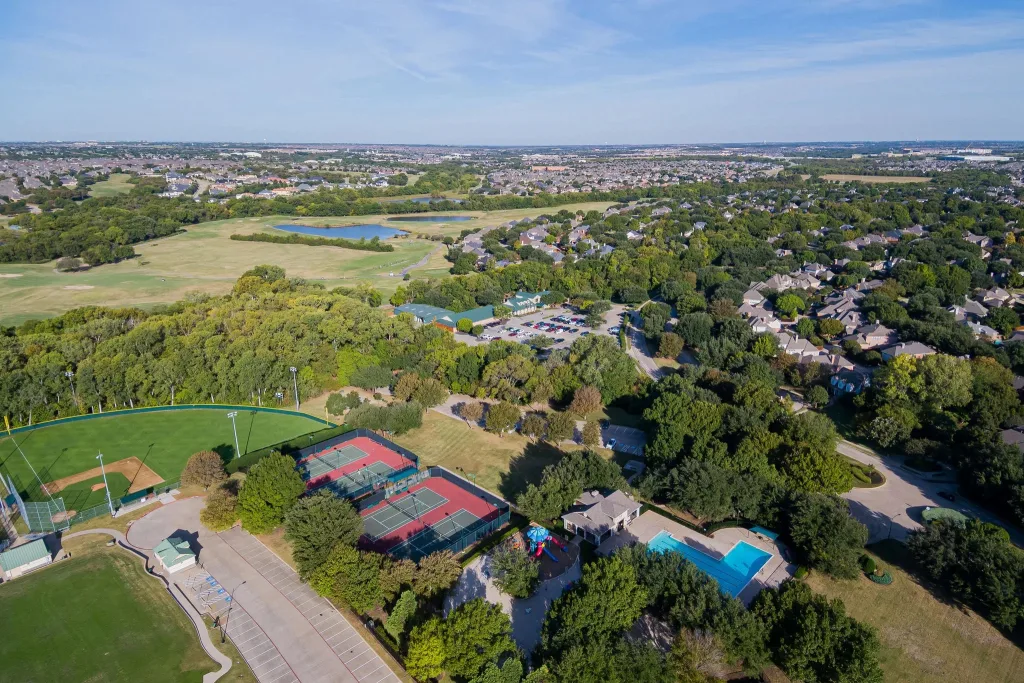 Overhead shot of a tennis court nestled within a picturesque neighborhood, highlighting homes and lush surroundings in Allen TX.