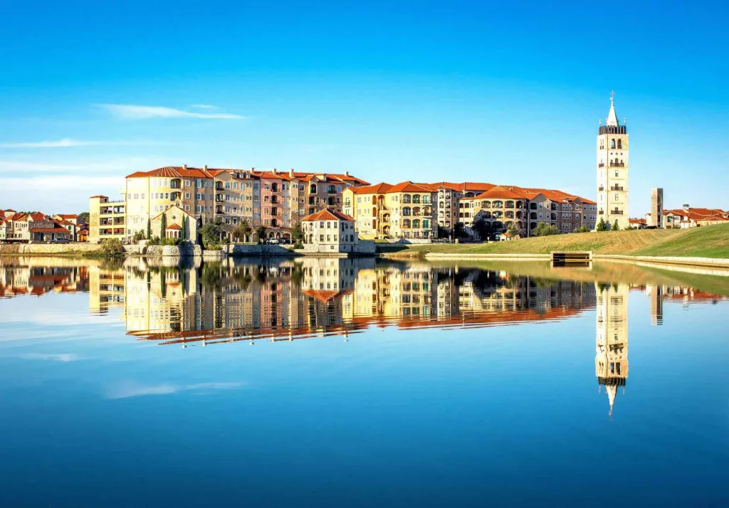 A serene lake reflecting buildings and a charming clock tower in the background, creating a picturesque scene.
