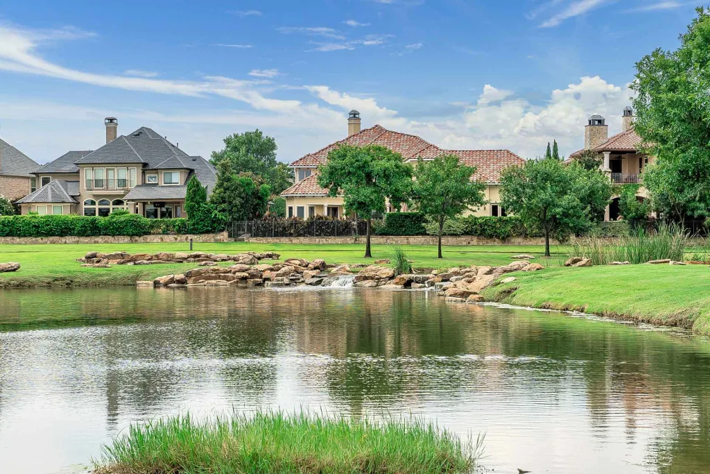 A serene pond surrounded by a vibrant green field, with charming houses nestled in the background.
